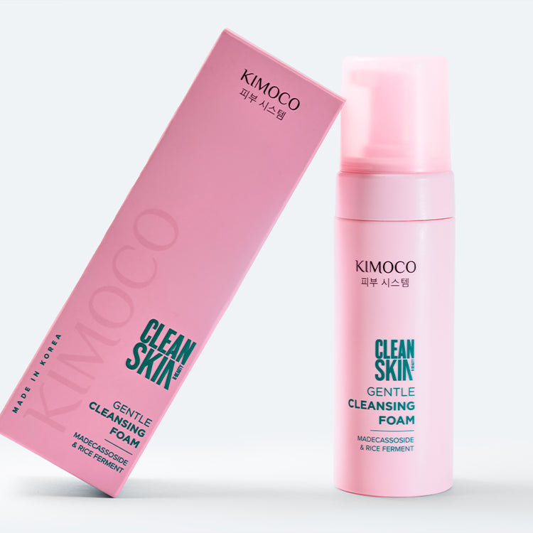 Po środku różowa butelka kosmetyku Kimoco Clean Skin Gentle Cleansing Foam z białą pianką przy pompce i przy dnie, na białym tle.