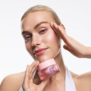 Twarz kobiety z dłonią przy policzku, trzymająca przy podbródku różowy słoiczek kosmetyku Kimoco Lift-Up Skin Pepti-Lift Night Firm Cream, na białym tle.