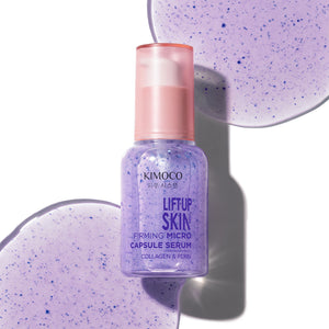 Po środku fioletowa butelka z pompką kosmetyku Kimoco Lift-Up Skin Firming Micro Capsule Serum, na tle dużych fioletowych kropli z kapsułkami.