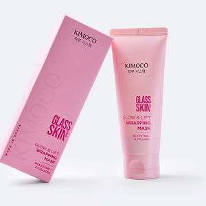 Różowe pudełko oparte o różową tubę kosmetyku Glass Skin Glow & Lift Wrapping Mask, na szarym tle.