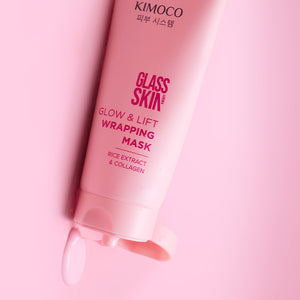 Zbliżenie na różową tubkę kosmetyku Kimoco Glass Skin Glow & Lift Wrapping Mask z ekstraktem ryżowym i kolagenem, z otwartej zakrętki wypływa kropla produktu, na różowym tle